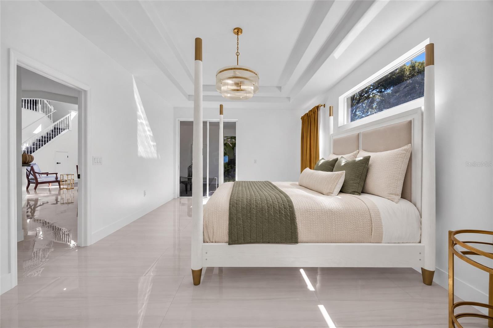 Staged bedroom with a white bed, olive accents, glossy tile floors, and a tray ceiling.