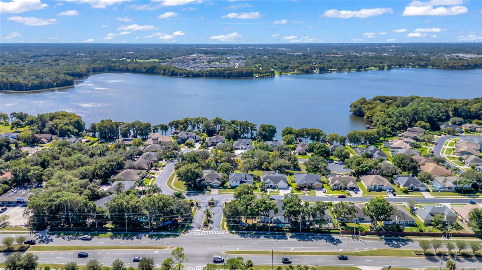 Aerial view of homes beside a broad lake, with wooded shorelines and a road in the foreground.