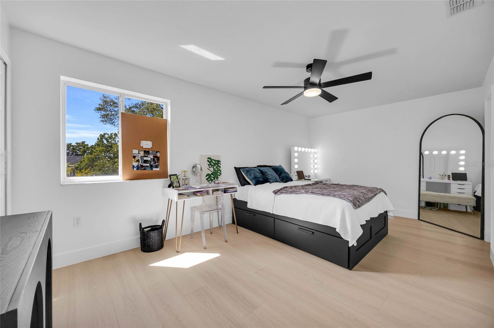 Furnished bedroom with a black platform bed, vanity desk, and large window.