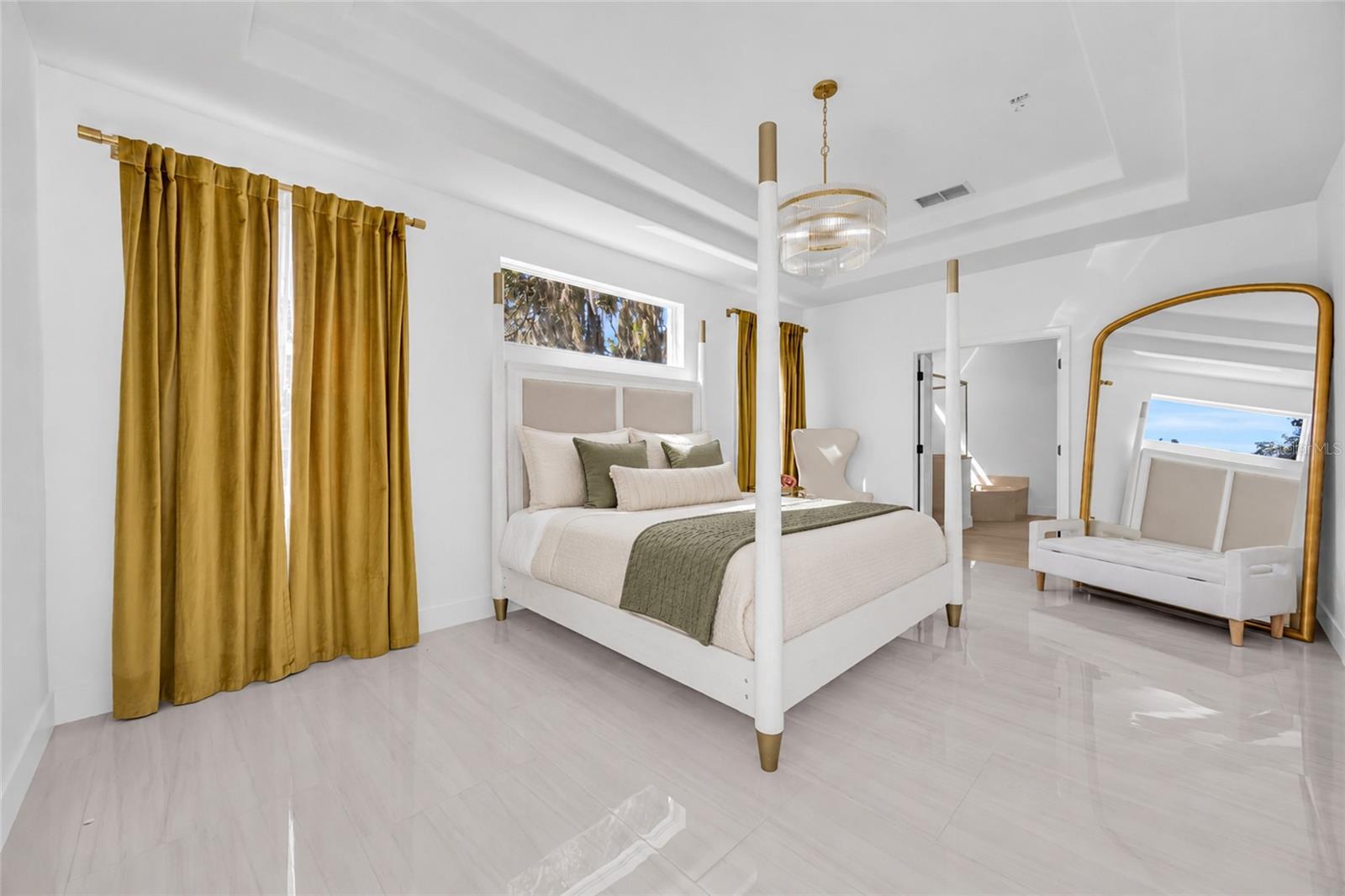 Staged bedroom with a white canopy bed, gold curtains, and a large arched mirror.