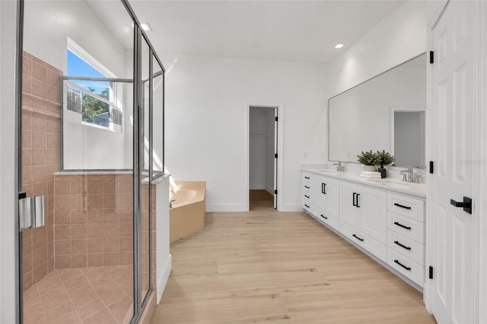 Primary bathroom with a tiled glass shower, soaking tub, and long double vanity.