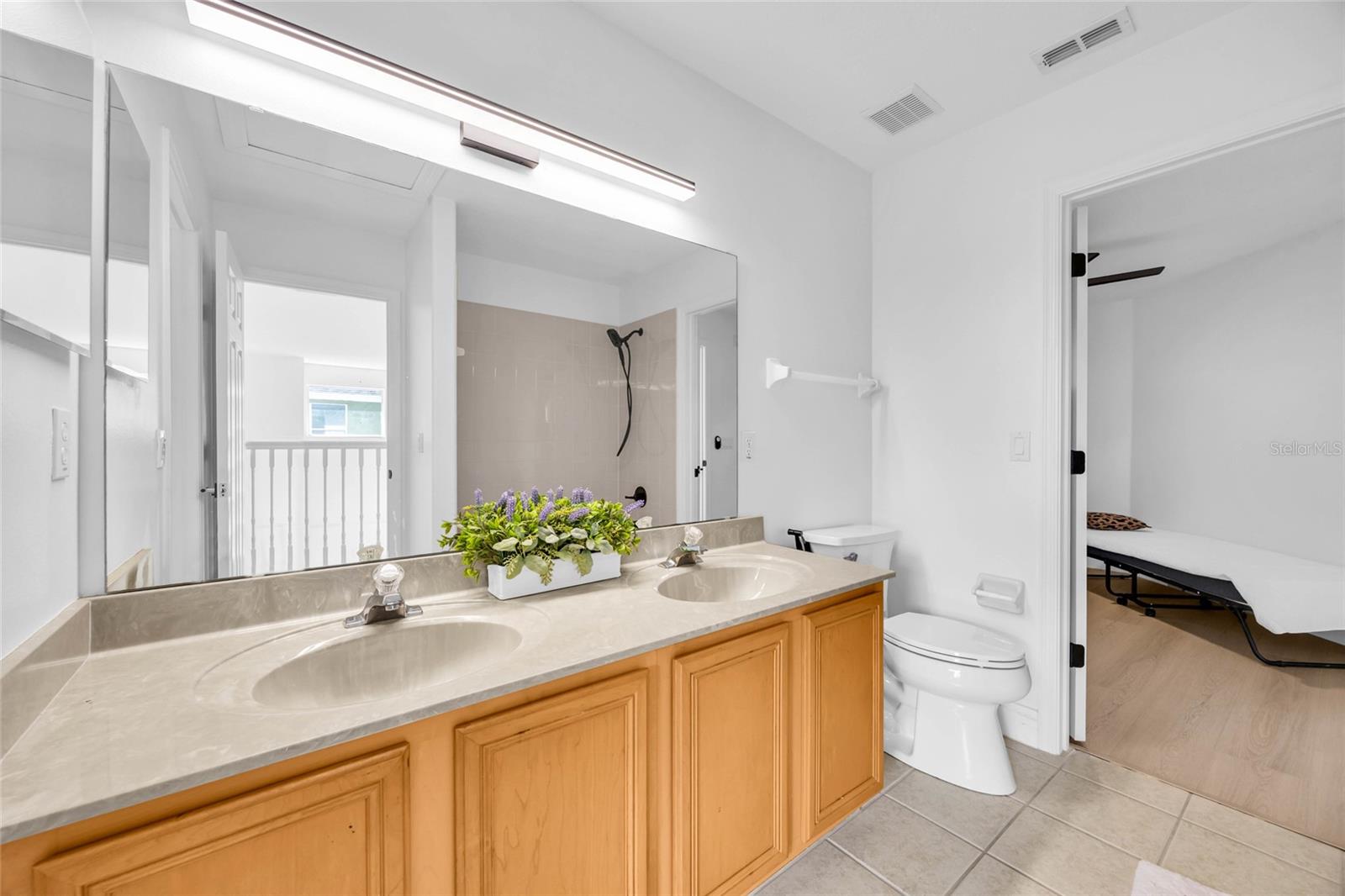 Bathroom with a long double vanity, wood cabinetry, large mirror, and tiled shower.