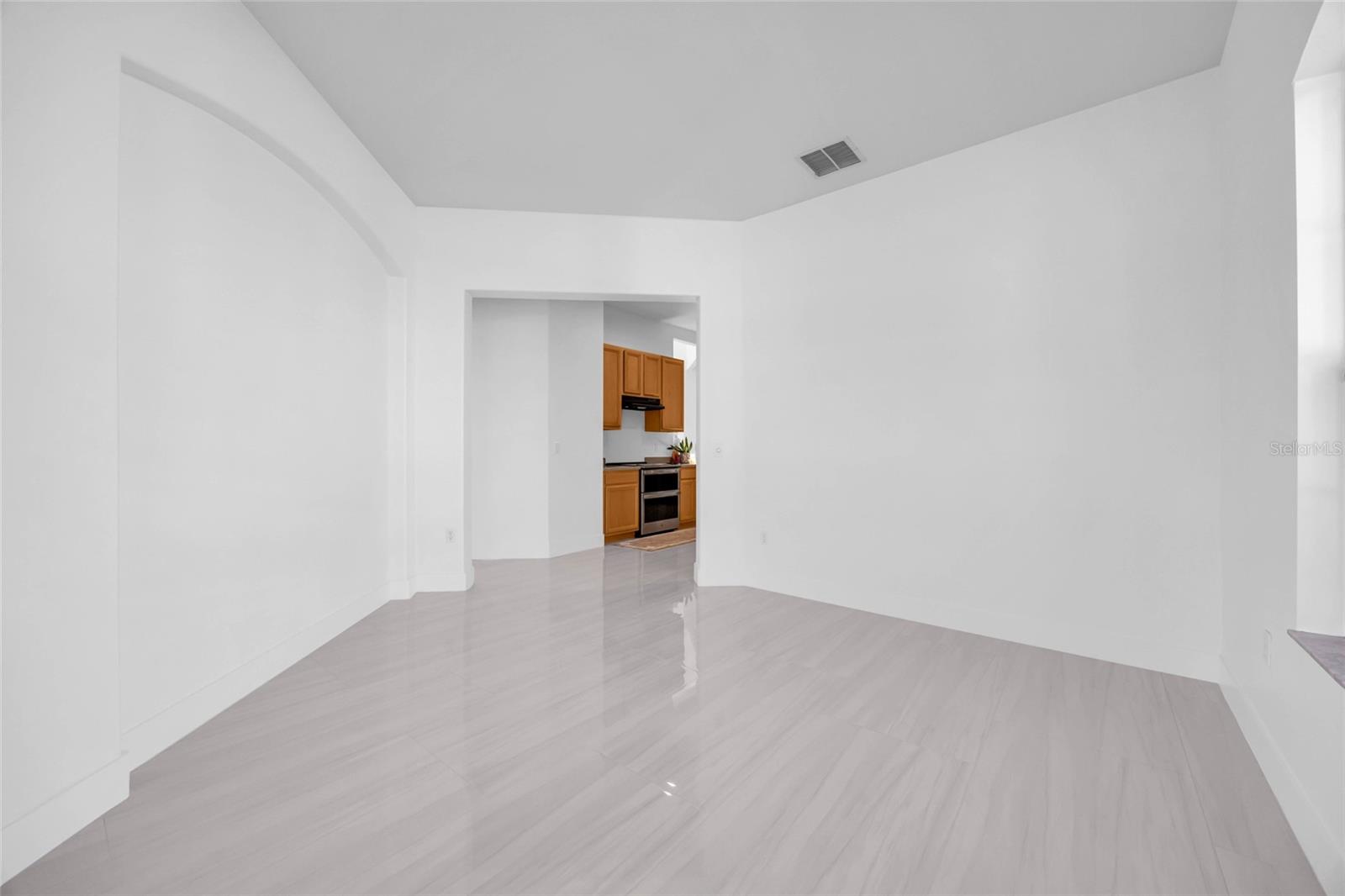 Vacant living area with pale flooring, a tray ceiling, and a view into the kitchen.
