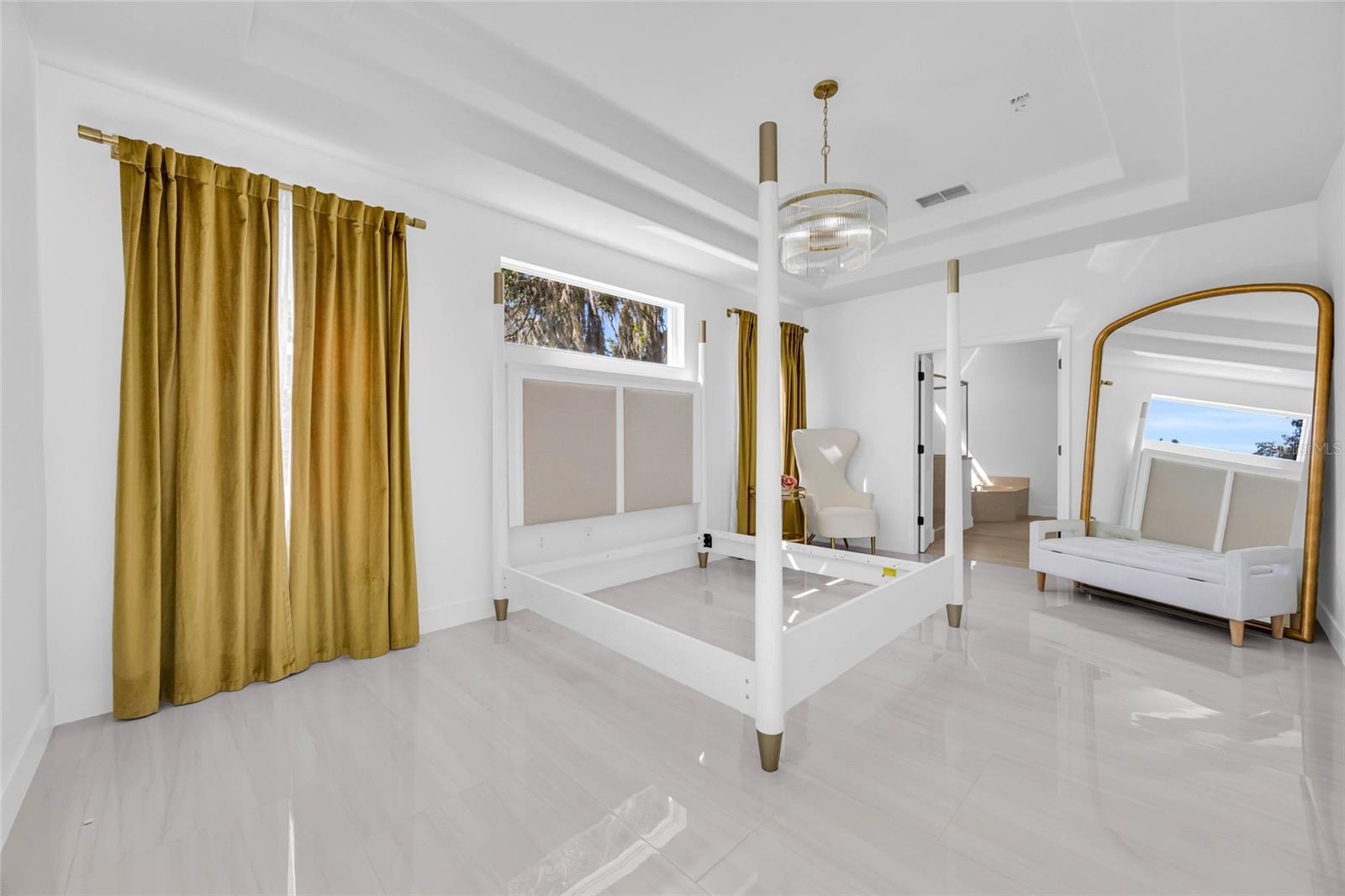 Bright white bedroom with a four-poster bed frame, gold curtains, and a large gold-framed mirror.