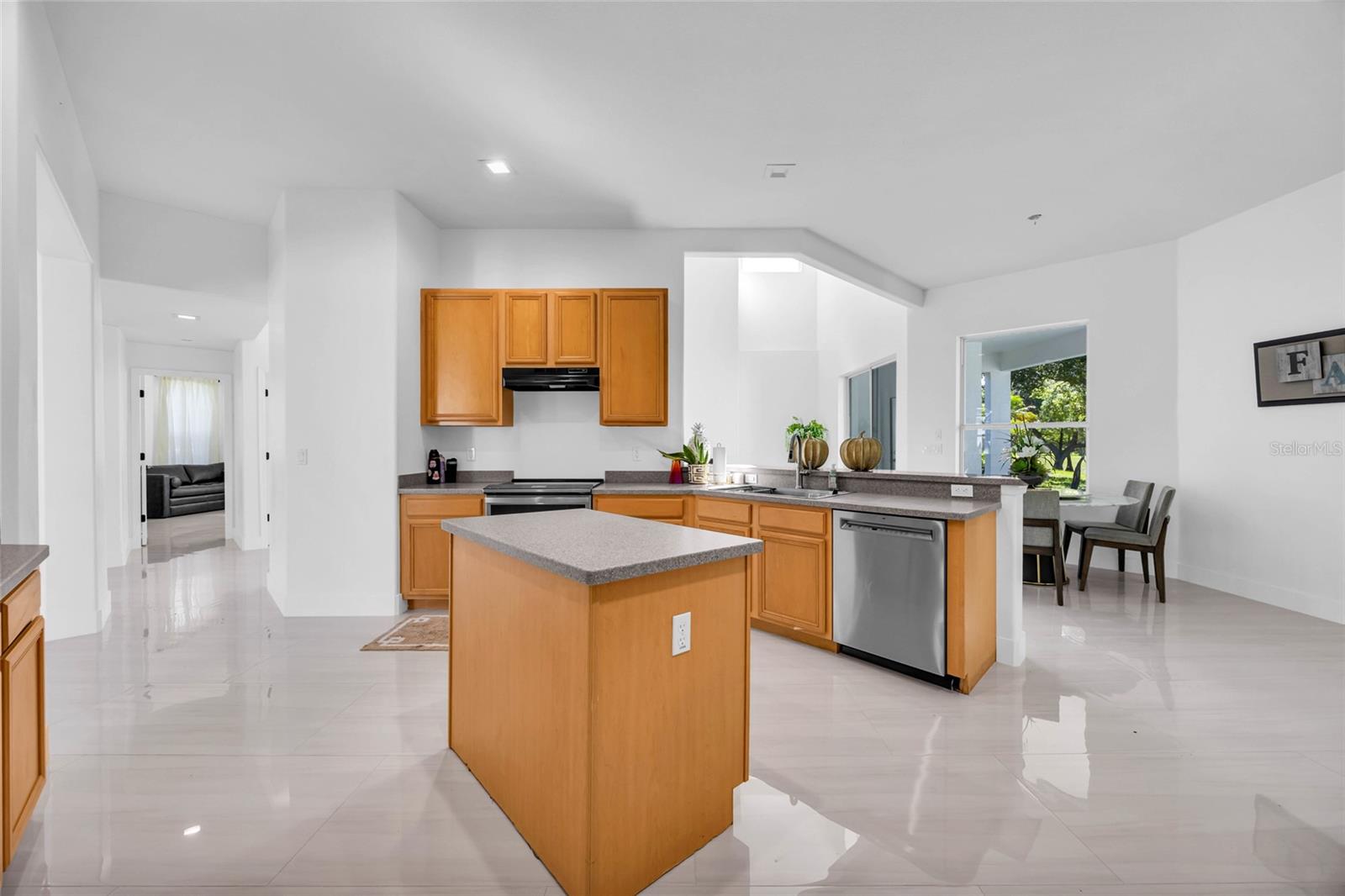 Kitchen with a central island, honey-colored cabinets, gray countertops, and a dining area by the window.