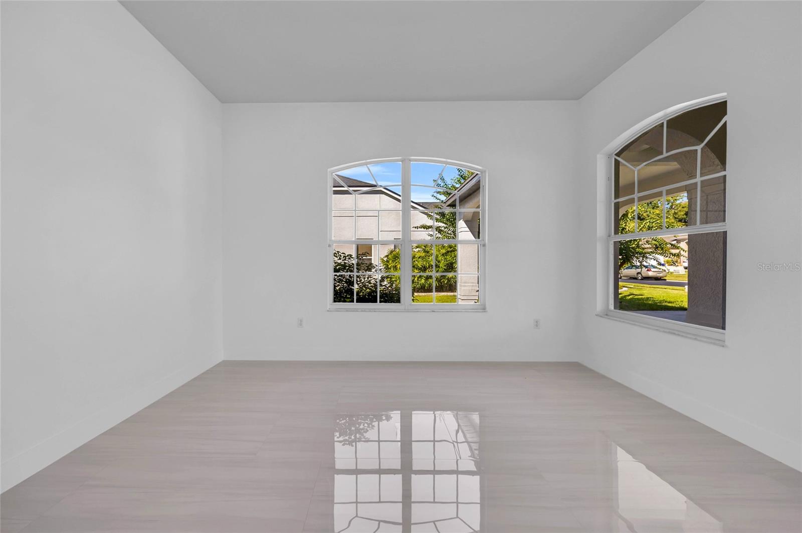 Vacant room with glossy light tile floors and two arched grid-paned windows.