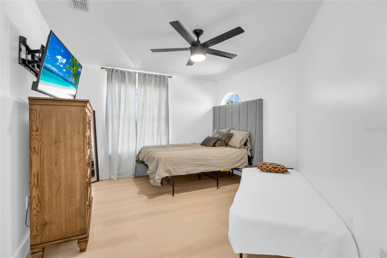 Bedroom with two beds, a gray upholstered headboard, and a wall-mounted television.