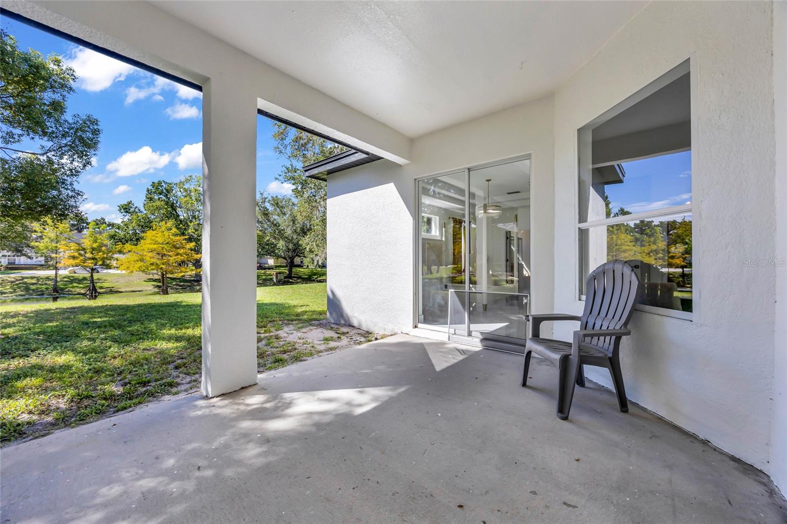 Covered patio with sliding glass doors, a gray chair, and a tree-lined grassy yard.