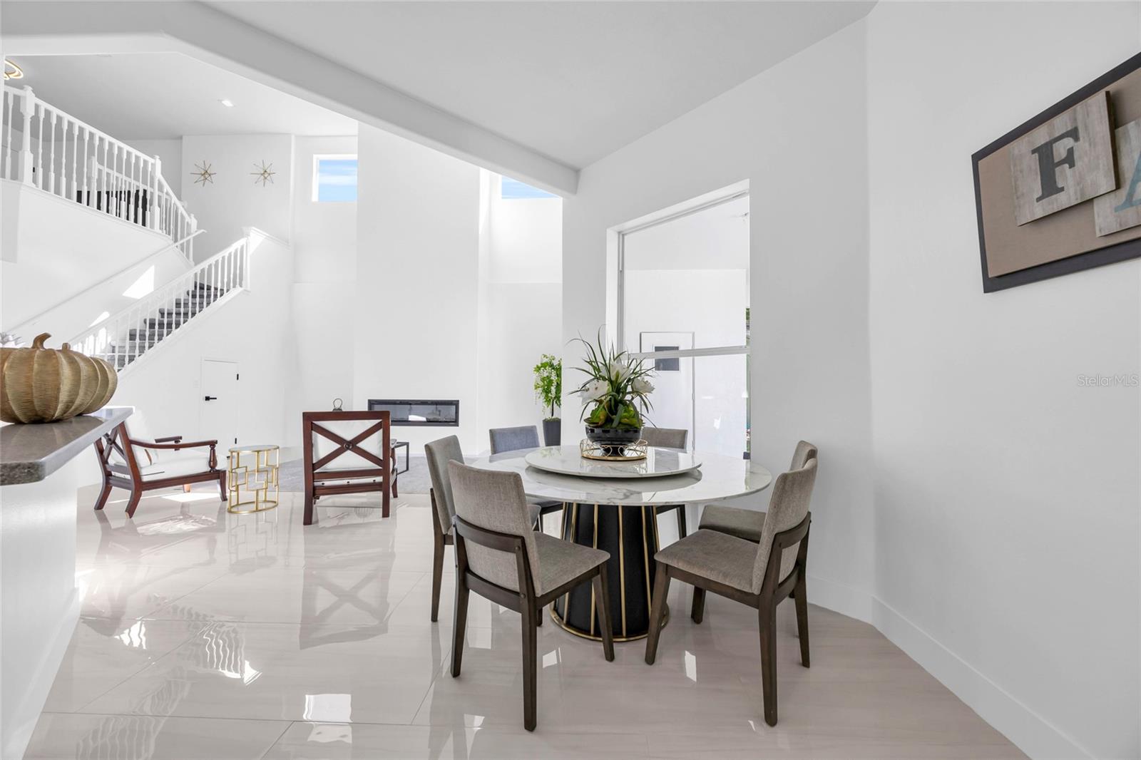 Dining area with a round table, glossy tile floors, and a white staircase with loft railing.