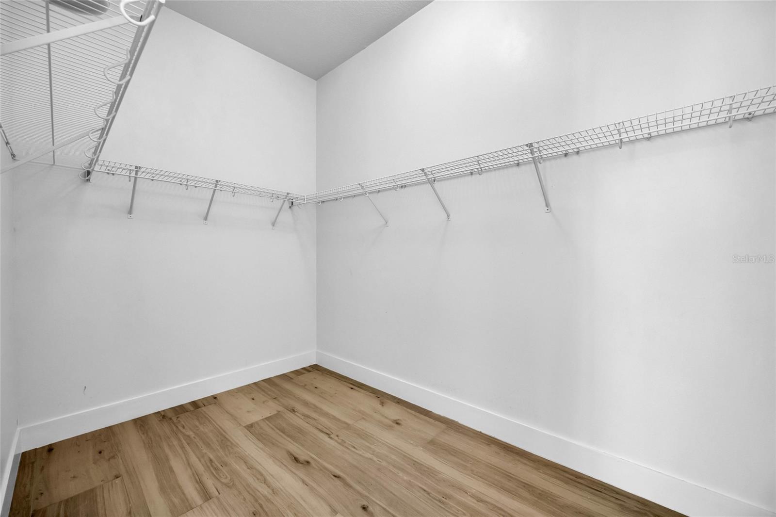 Empty walk-in closet with white wire shelving and wood-look plank flooring.