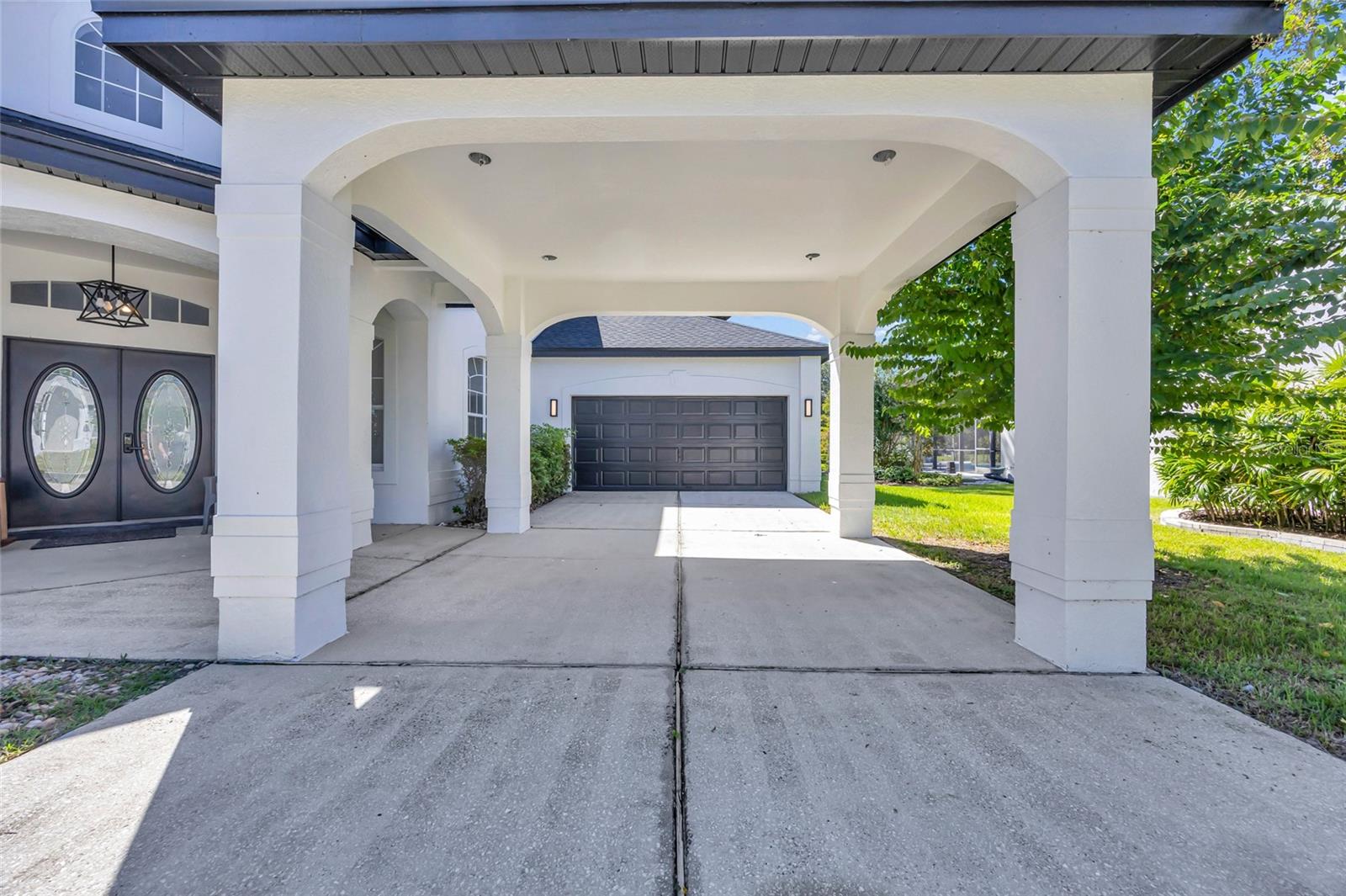 White home with a columned covered driveway, oval-glass double doors, and a dark double garage door.