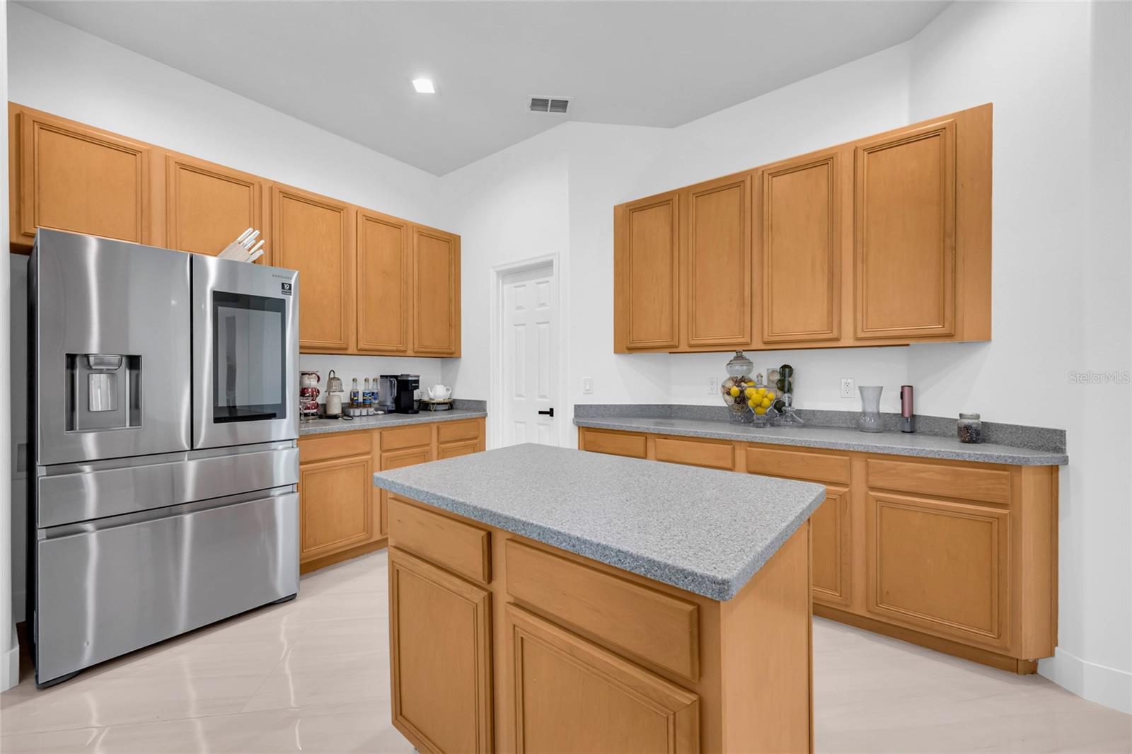 Kitchen with light wood cabinets, a central island, and a stainless steel refrigerator.