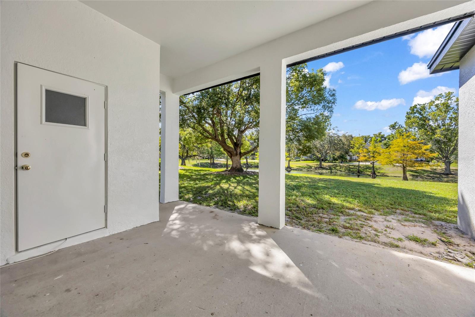 Covered patio overlooking a grassy yard, mature trees, and a small pond.