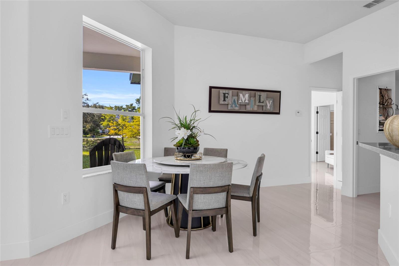 Dining area with a round table and gray chairs beside a large window overlooking the yard.
