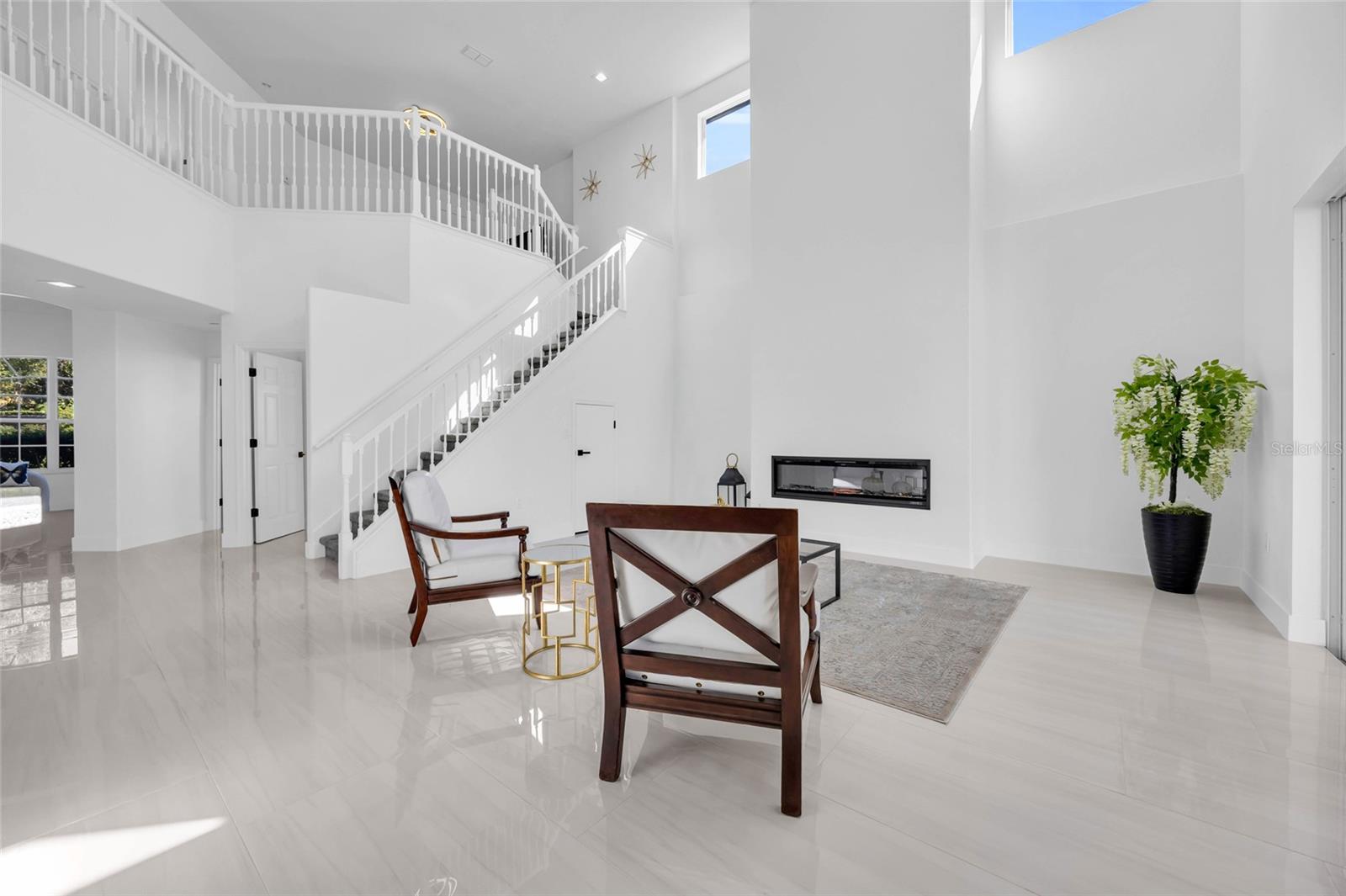 Double-height living room with a sweeping staircase, linear fireplace, and contemporary seating.