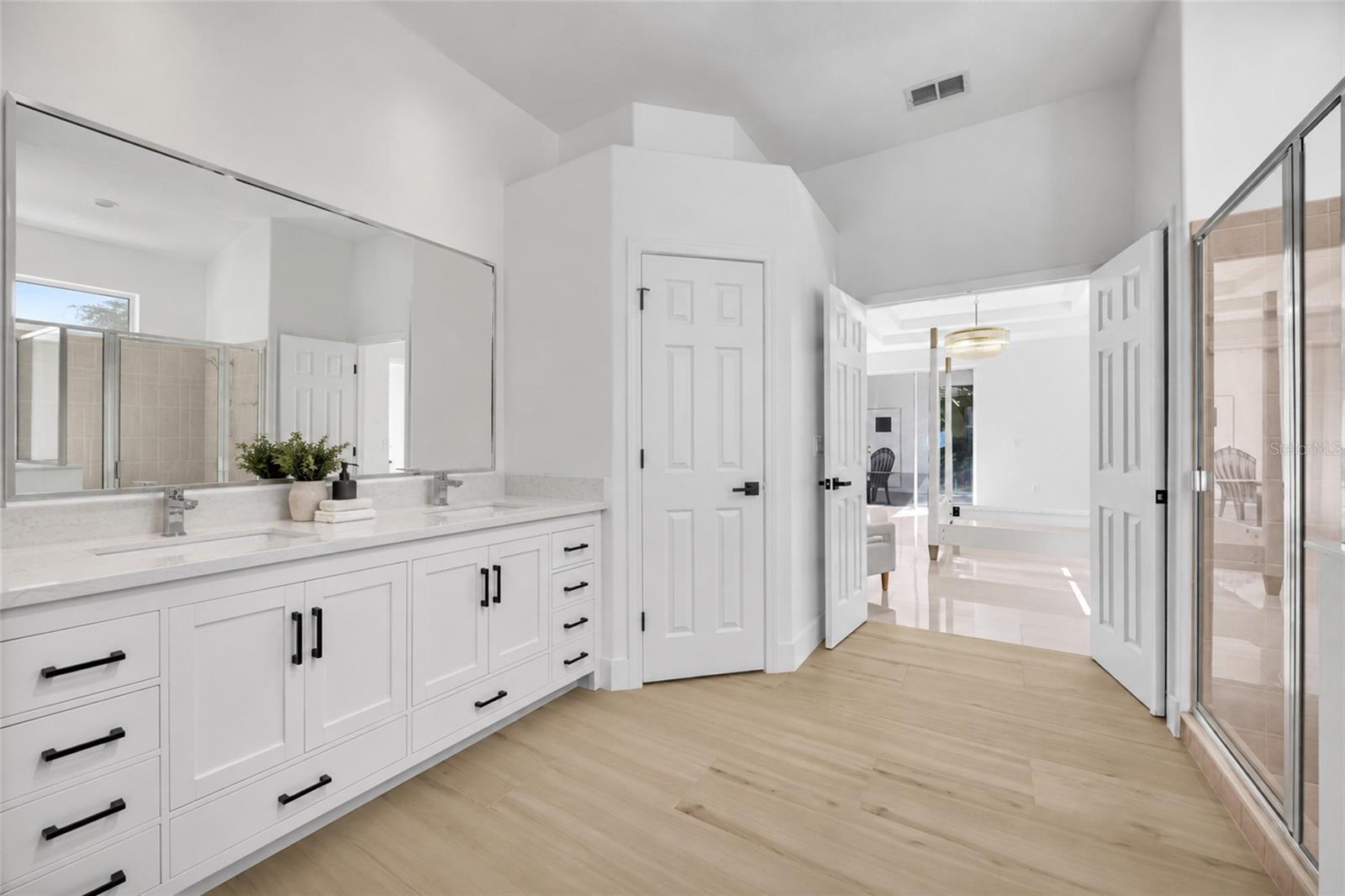 Bright bathroom with a long white vanity, large mirrors, and glass-enclosed shower.