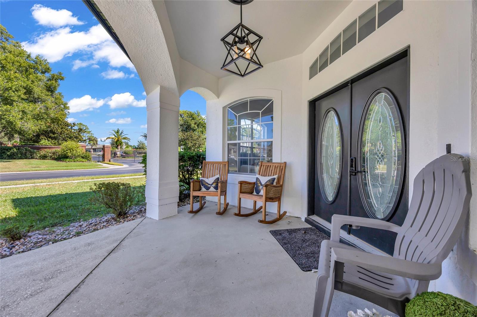 Covered front porch with arched columns, oval-glass double doors, and two wooden rocking chairs.