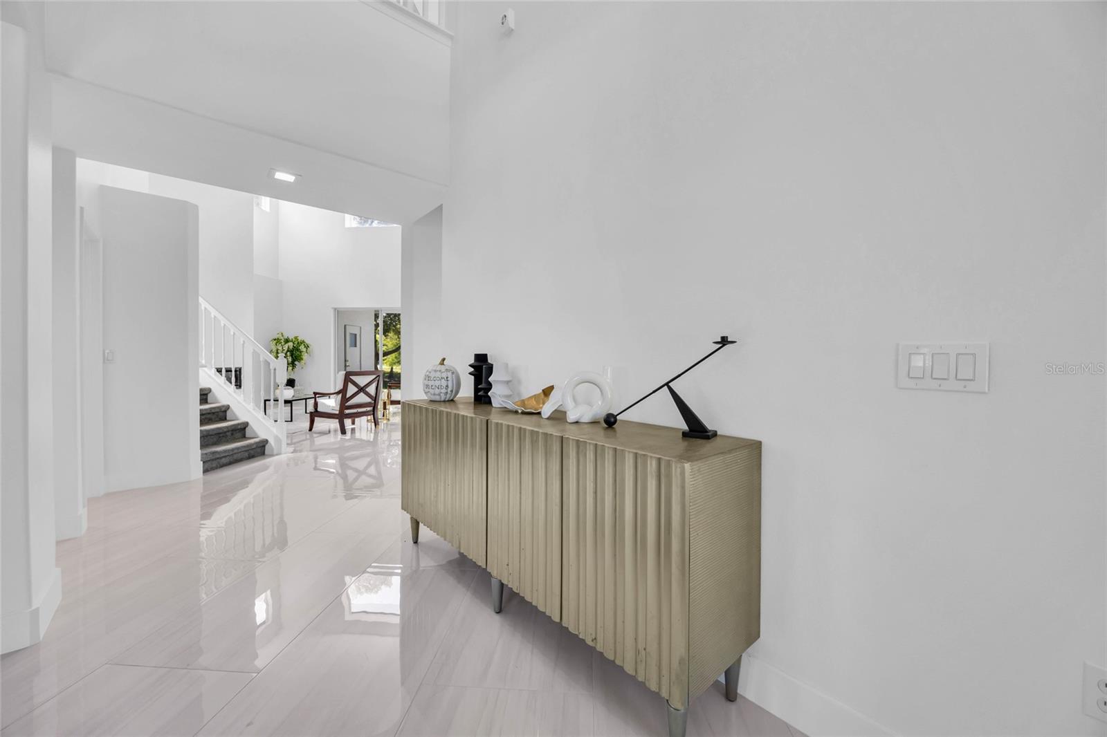 Bright entry hall with glossy white tile, a carpeted staircase, and a fluted console cabinet.
