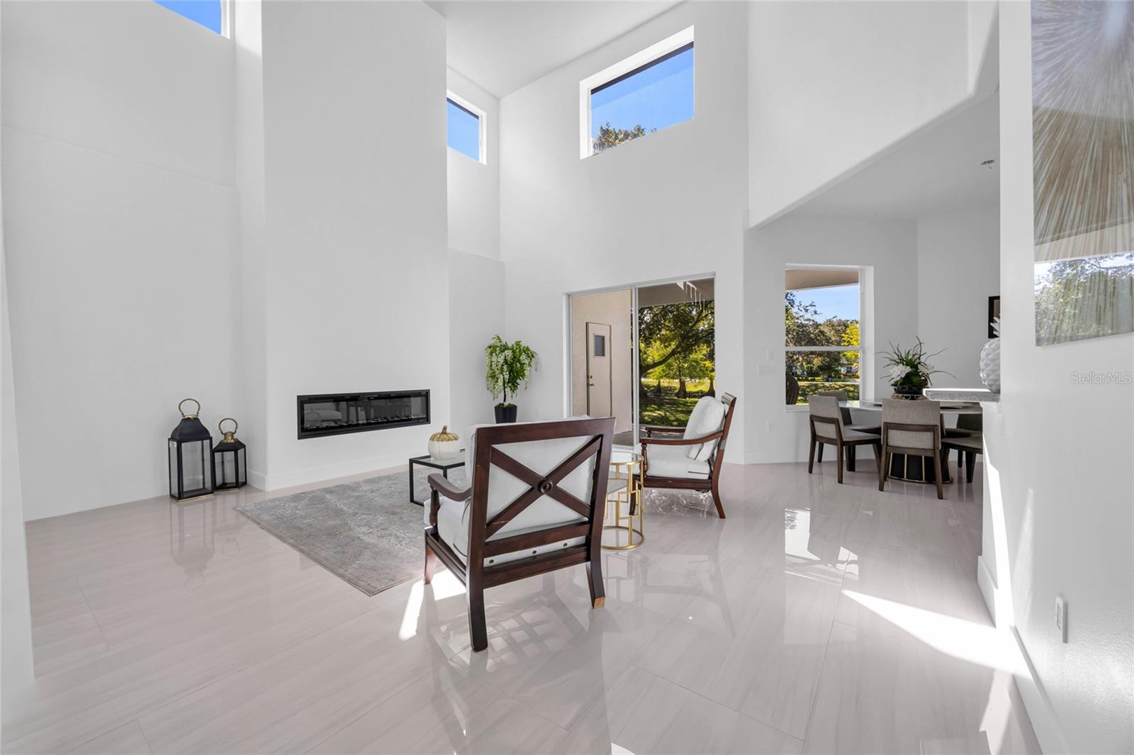 Two-story living room with soaring ceilings, a linear fireplace, glossy tile floors, and an adjoining dining area.