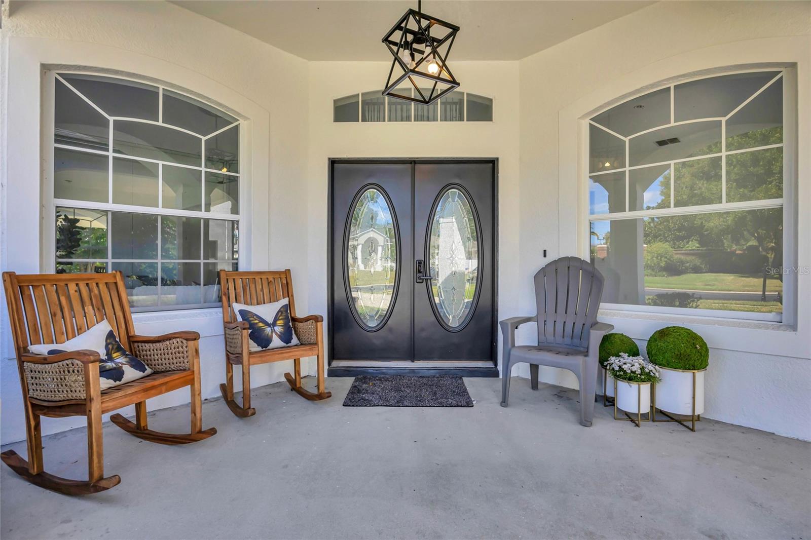 Covered front porch with oval-glass double doors, arched windows, and wooden rocking chairs.