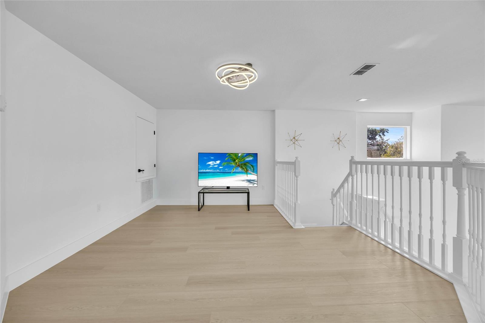 Bright upstairs loft with pale wood floors, white stair railings, and a television.