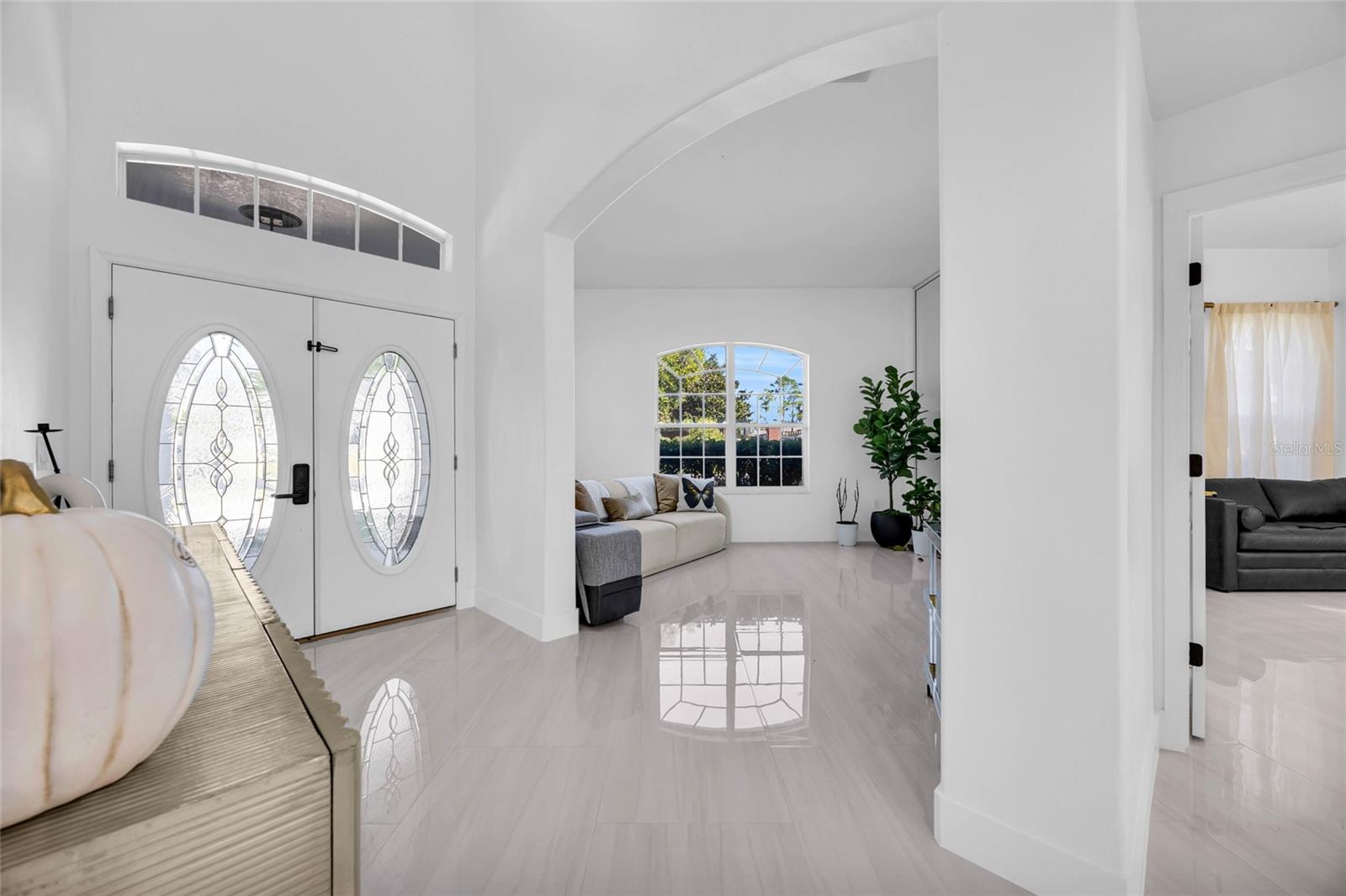 Bright entryway with decorative-glass double doors, an arched opening, and glossy tile floors.