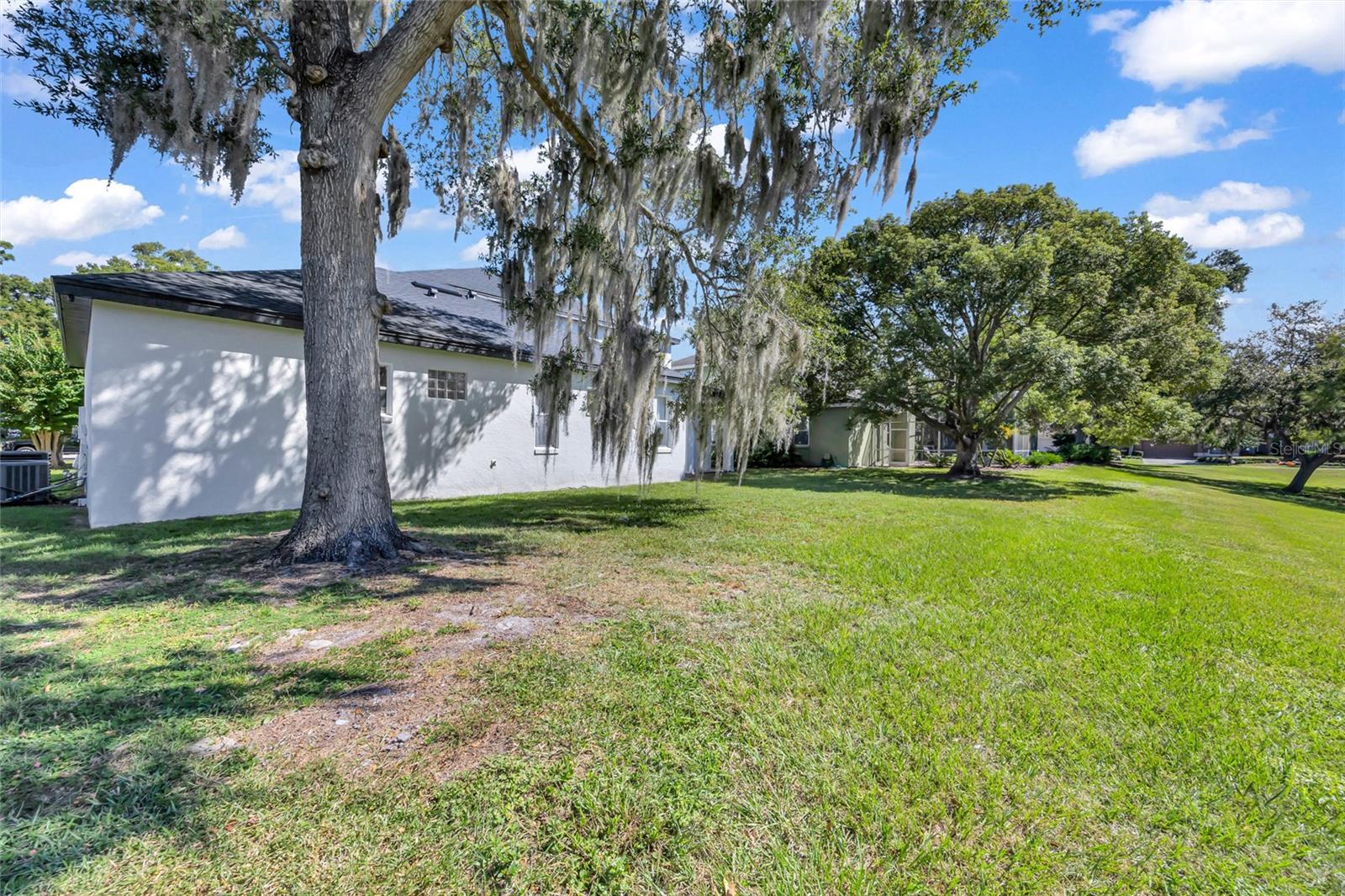 White home beside a broad grassy lawn, shaded by mature trees draped with Spanish moss.