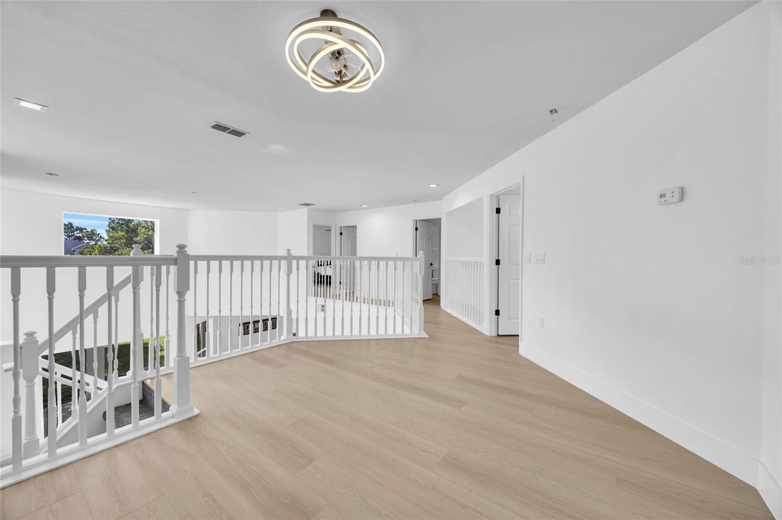Upstairs landing with pale wood-look flooring, white stair railing, and a modern circular ceiling light.