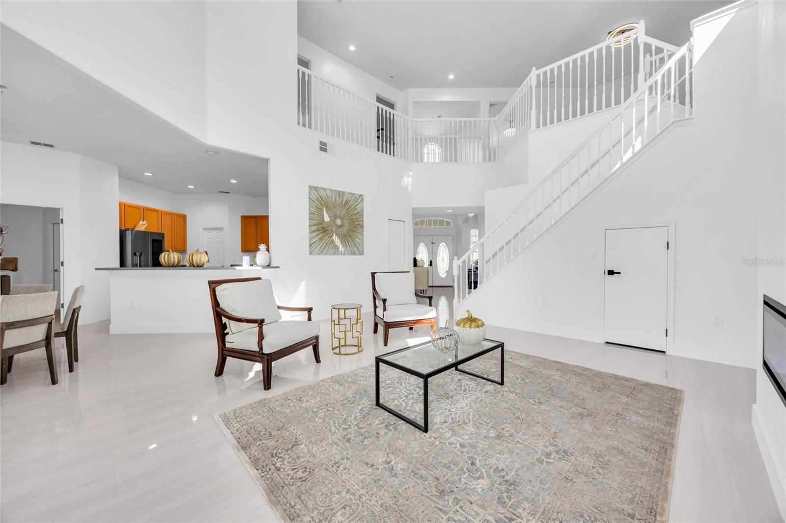 Staged living room with a patterned rug, open kitchen, and sweeping white staircase.
