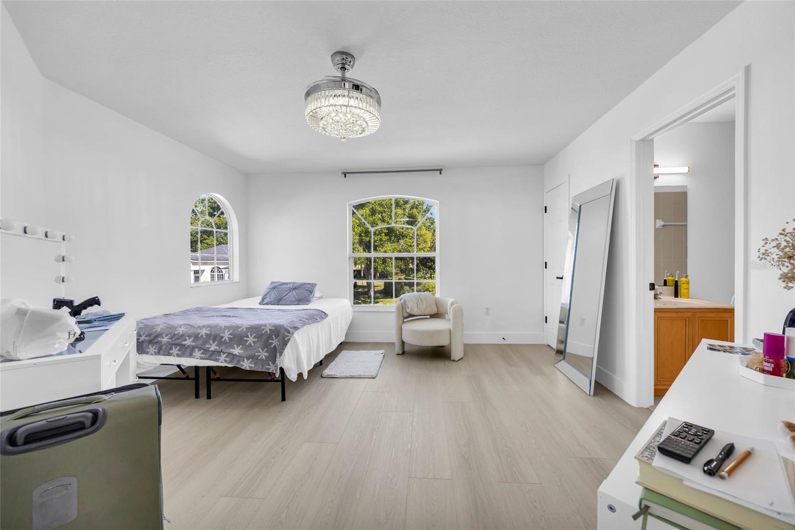 Bright bedroom with arched windows, a bed, crystal ceiling light, and an adjoining bathroom.