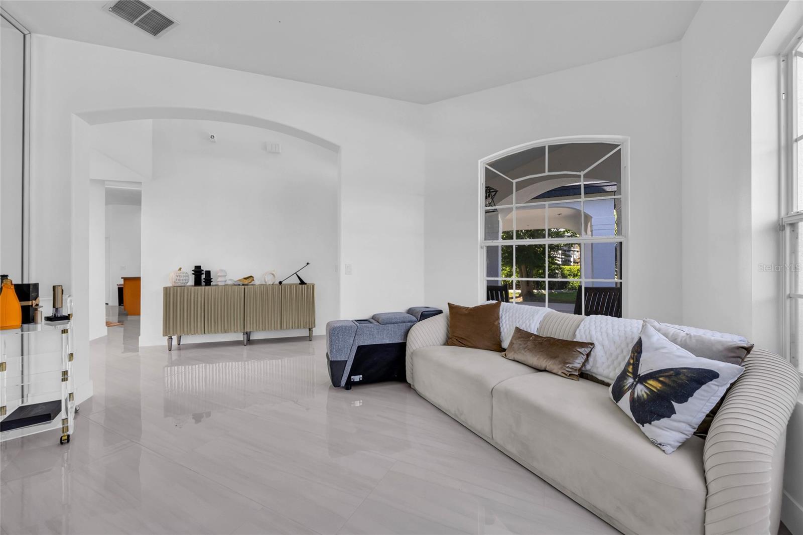 Furnished living room with a curved cream sofa, glossy white tile floors, and a large arched window.