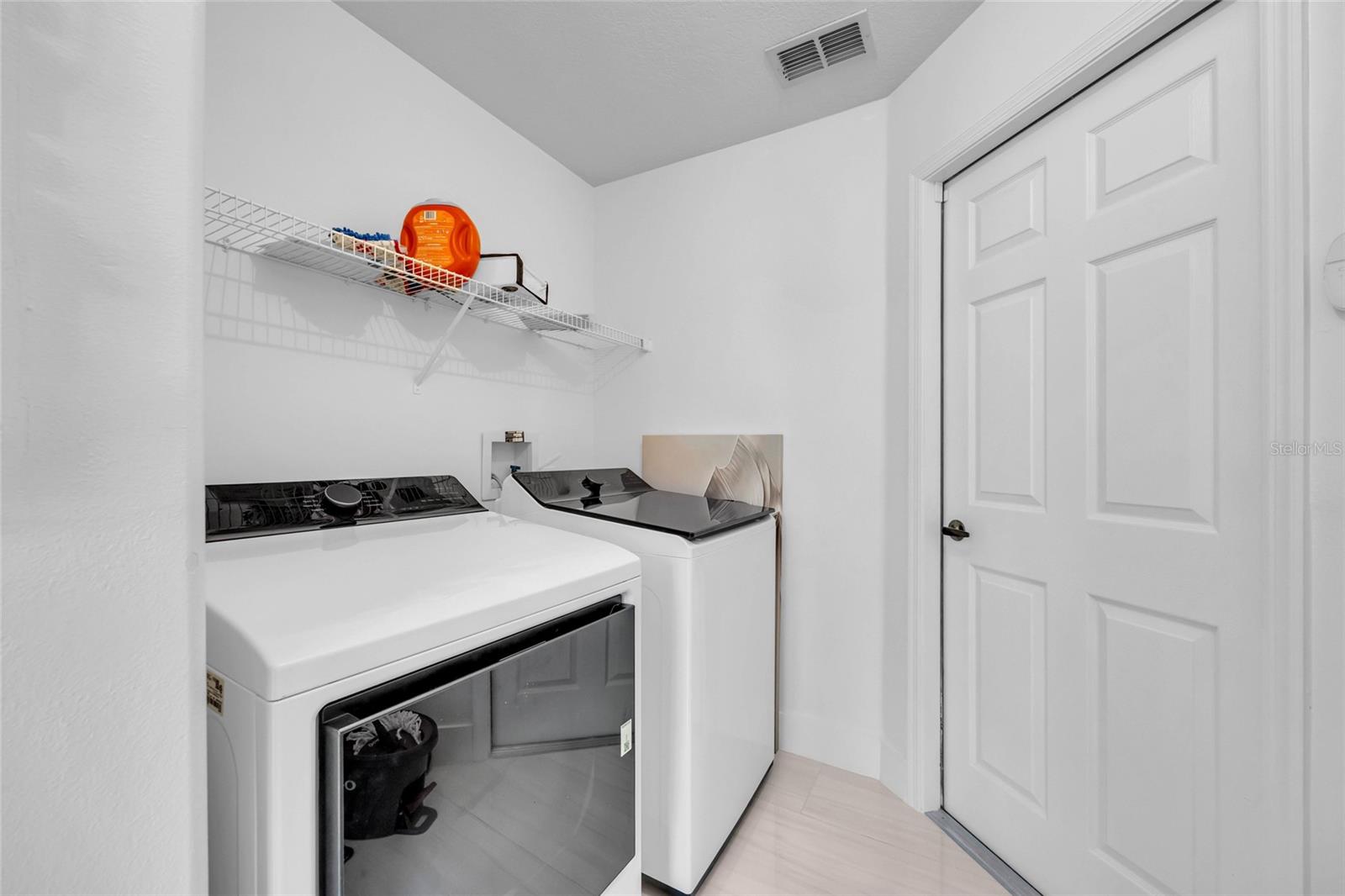 Laundry room with a front-loading dryer, top-loading washer, and wire storage shelf.