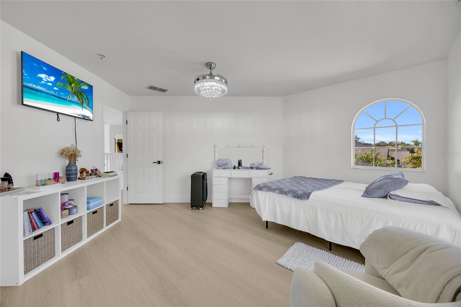 Furnished bedroom with a white bed, arched window, and light wood flooring.