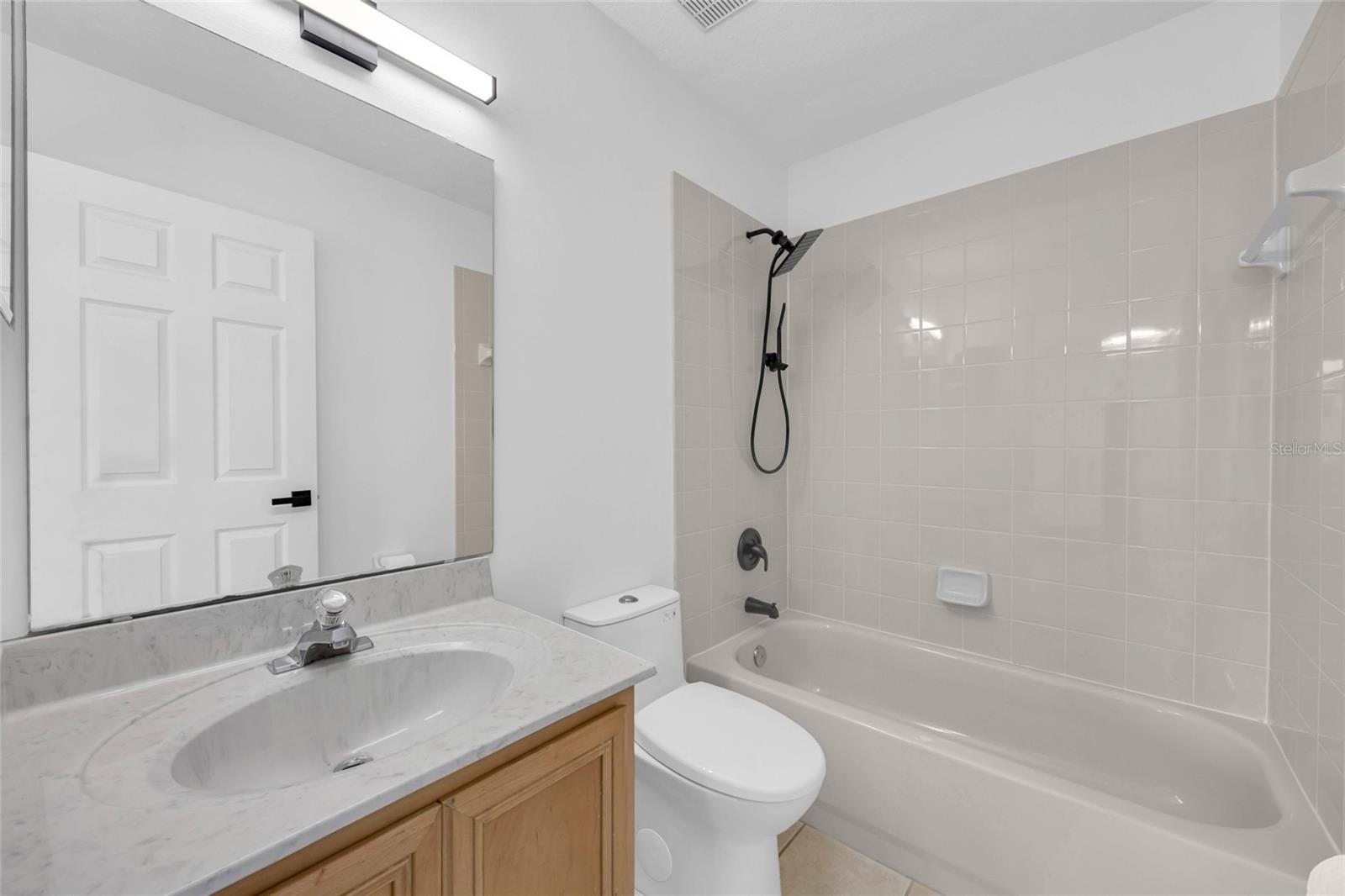 Bathroom with a tiled tub and black shower fixtures beside a marble-look vanity.