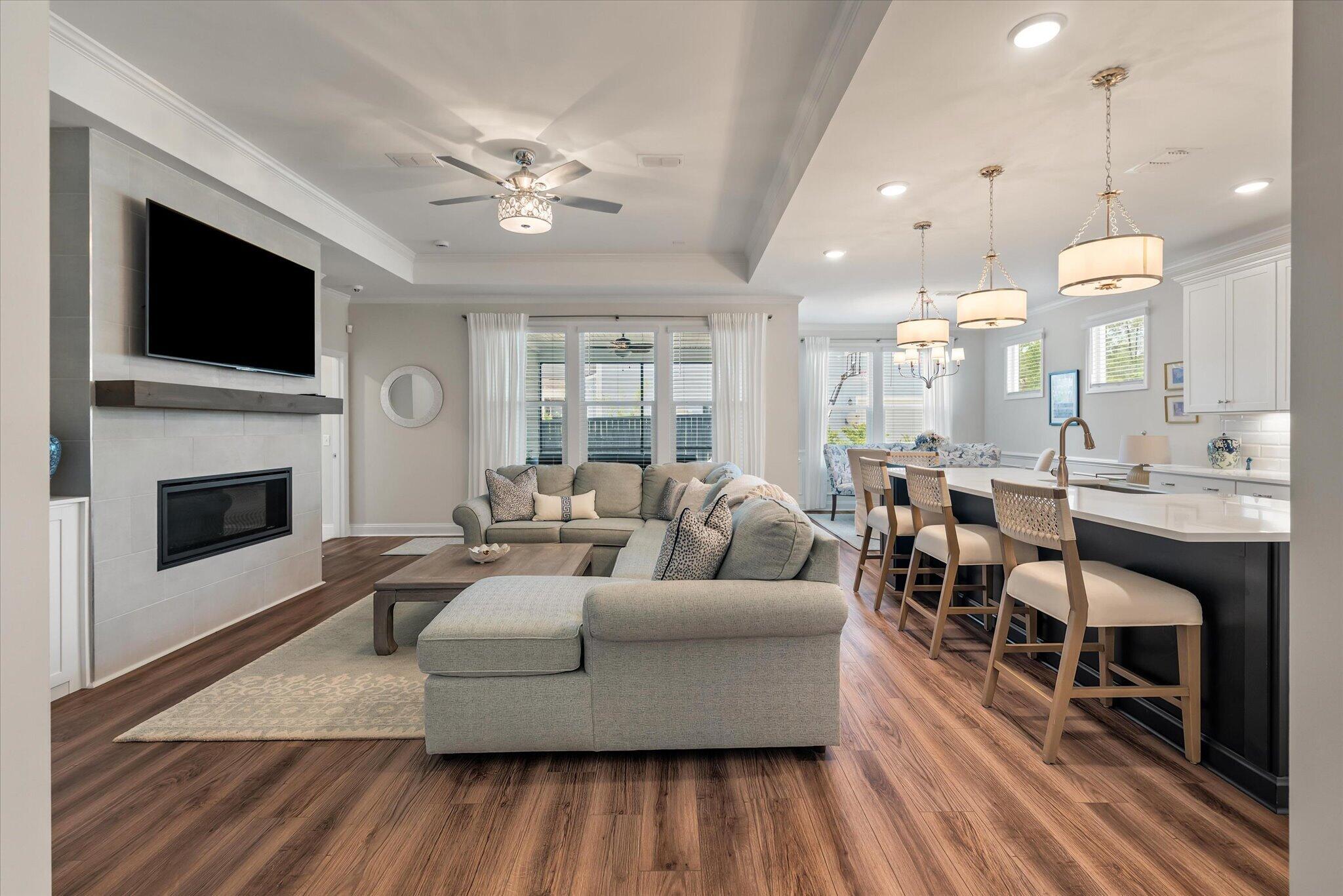 Open-plan living room with a gray sectional, tiled fireplace, and kitchen island with bar seating.