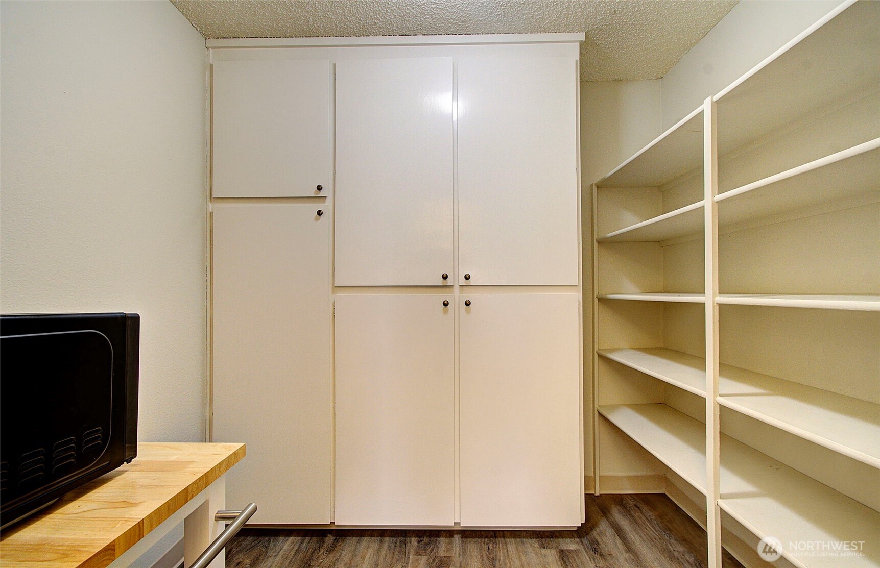 Built-in storage room with white cabinets, open shelving, and a wooden desk.