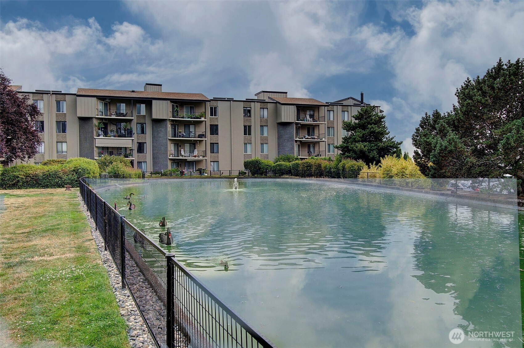 Condominium complex beside a fenced pond with ducks and landscaped grounds.