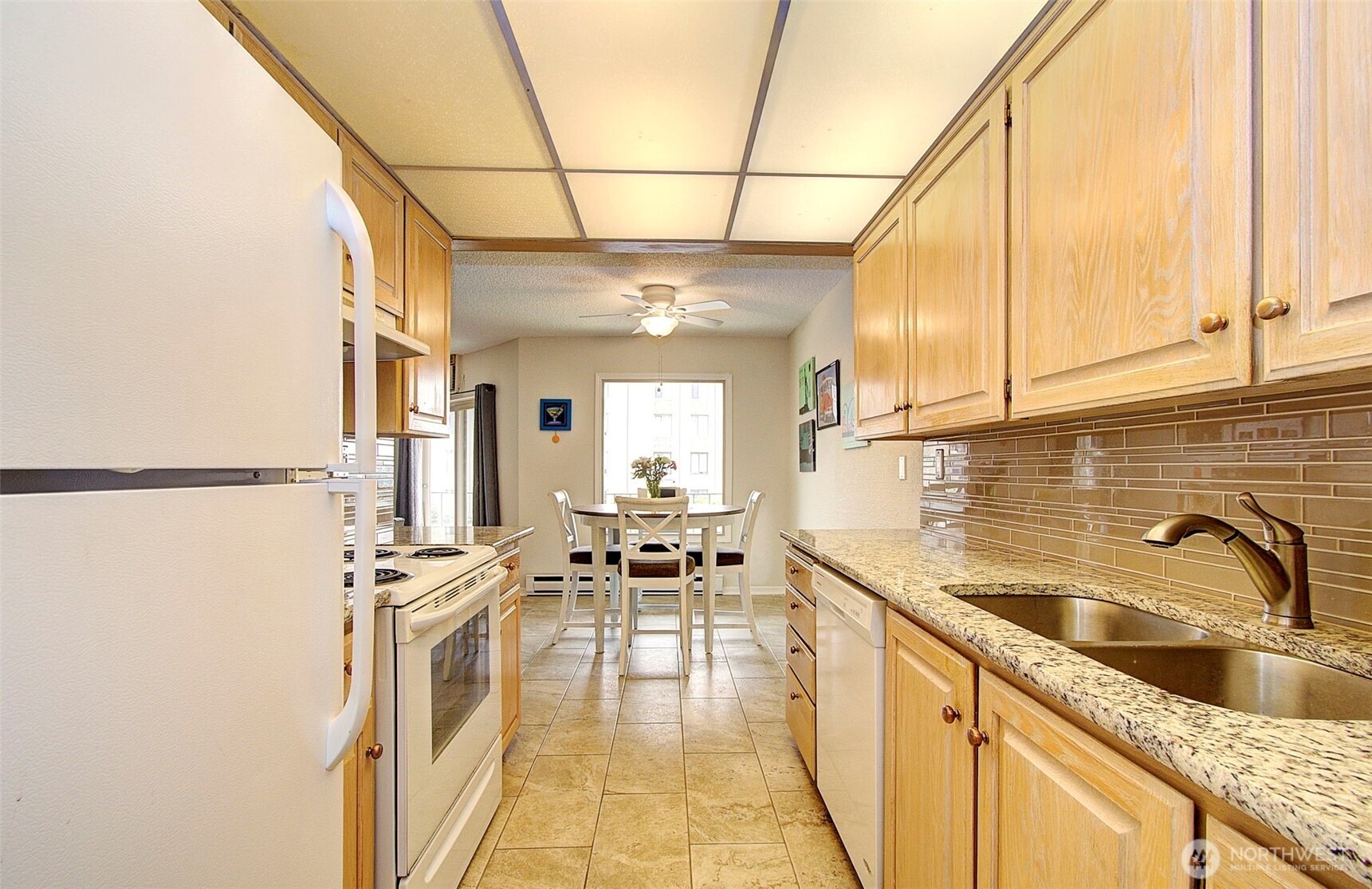 Galley kitchen with light wood cabinets, granite counters, and a dining table by the window.