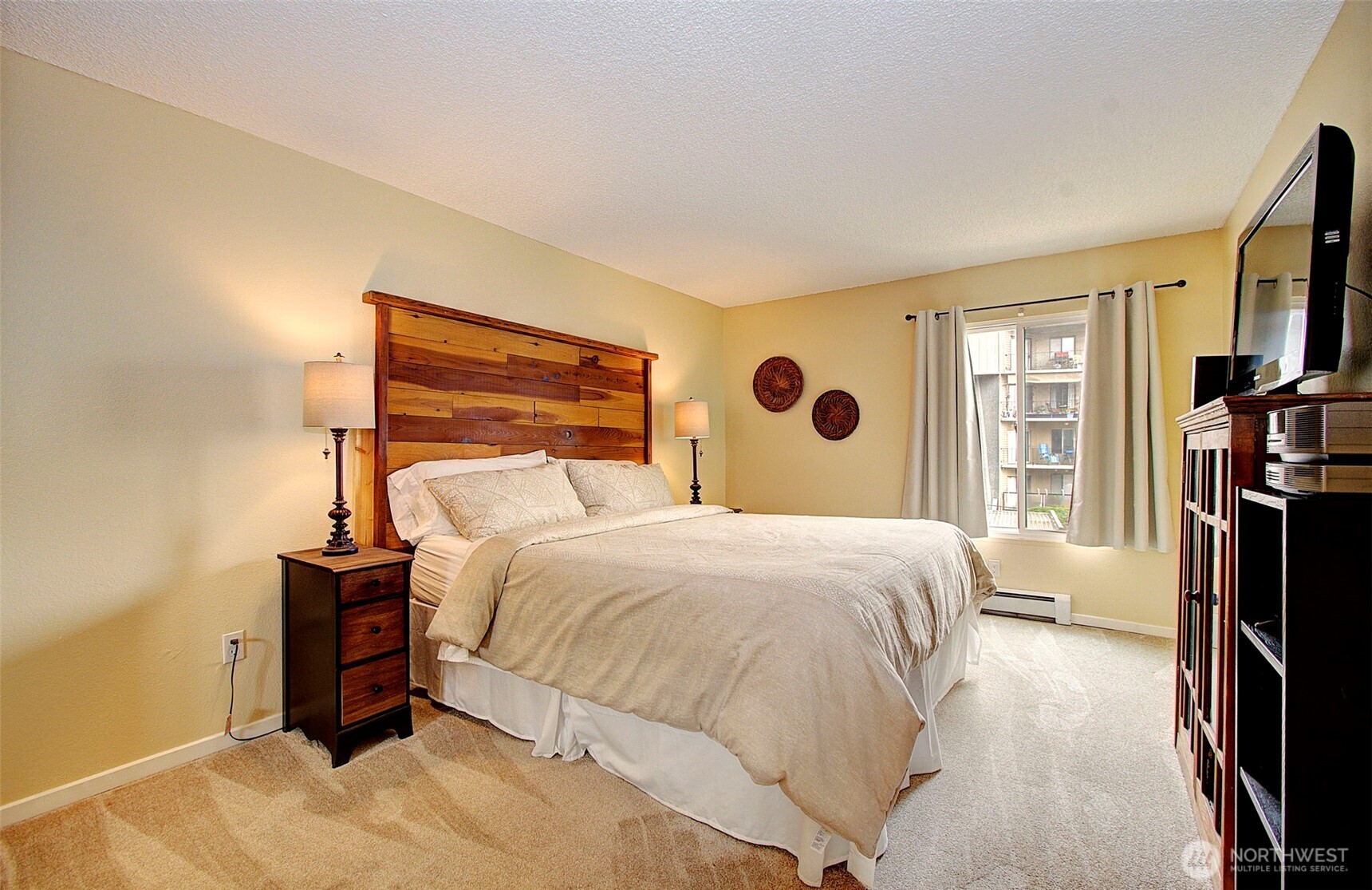 Furnished bedroom with a rustic wood headboard, neutral bedding, and a courtyard view.