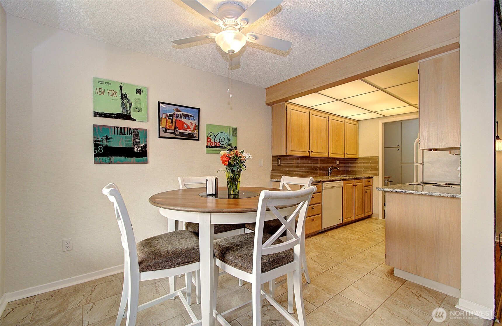 Dining area with a round table and white chairs beside a light wood kitchen.
