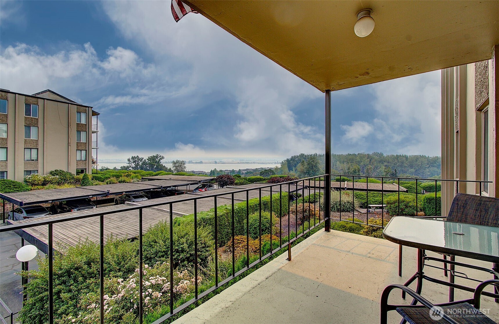 Condominium balcony overlooking landscaped grounds and a broad water view, with a patio table and chairs.