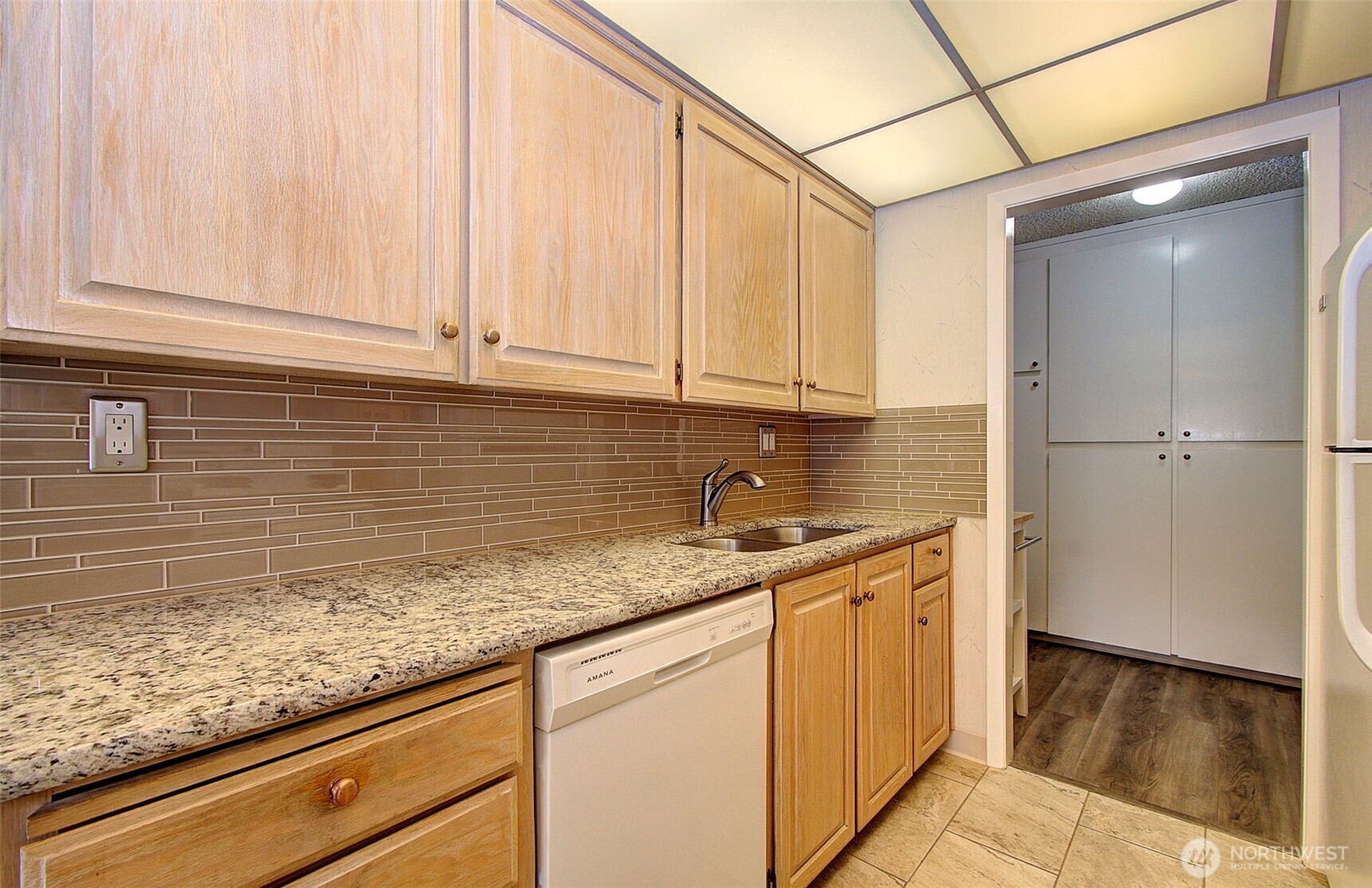 Kitchen with granite counters, light wood cabinets, brown tile backsplash, and a white dishwasher.