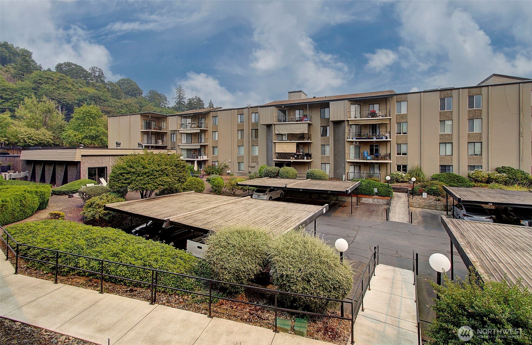 Multistory apartment building with balconies, landscaped grounds, and covered parking.