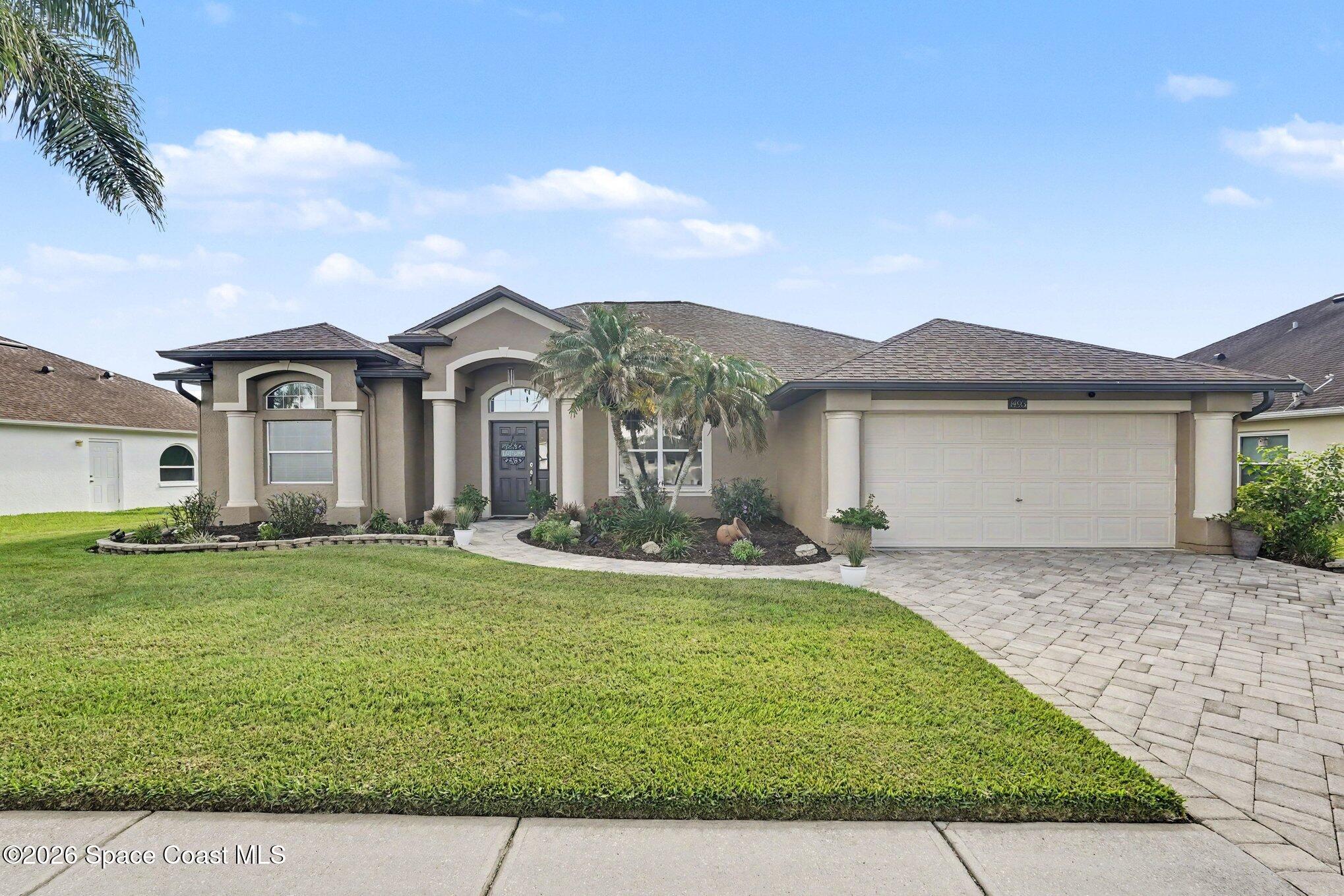 Single-story stucco home with a palm-lined entry, landscaped lawn, and wide paver driveway.