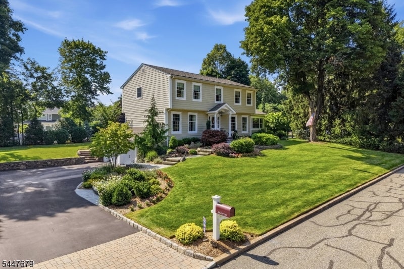 Beige two-story colonial house with a front porch, landscaped garden, and broad lawn.