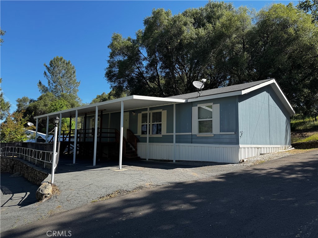 Blue manufactured home with white trim and a long covered carport beneath mature trees.
