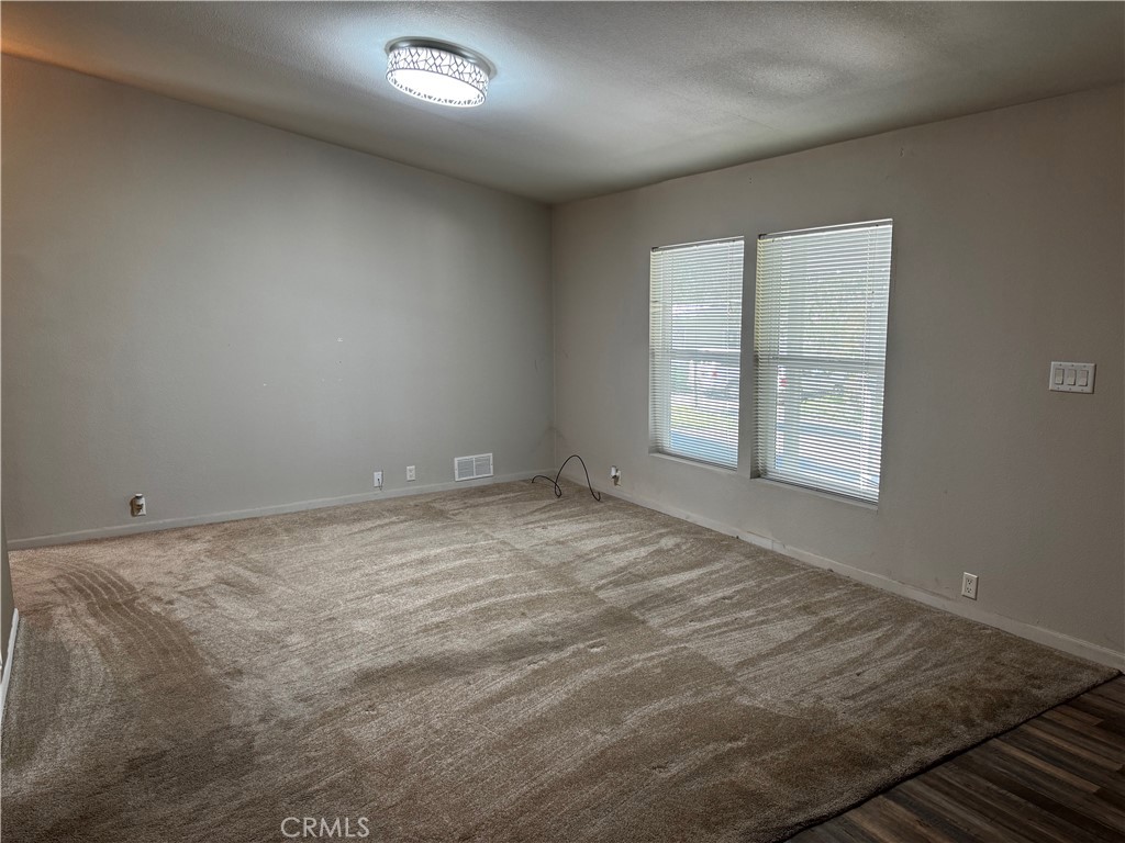 Empty carpeted room with gray walls, two windows with blinds, and a ceiling light.
