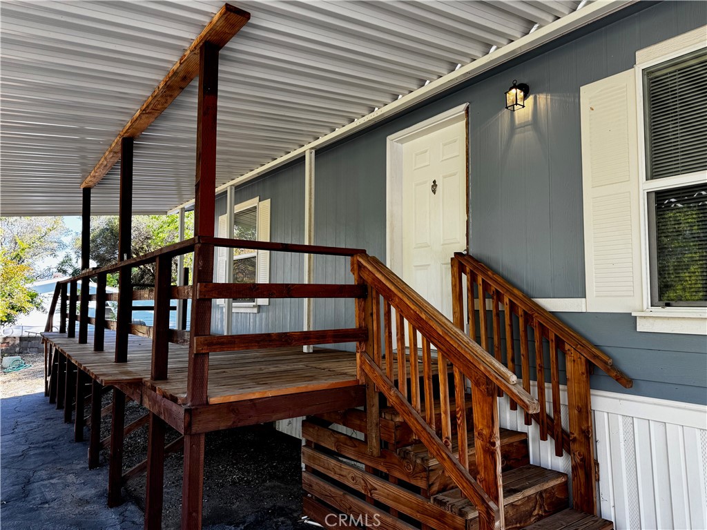 Covered wooden porch with dark railings and steps leading to a white entrance door.