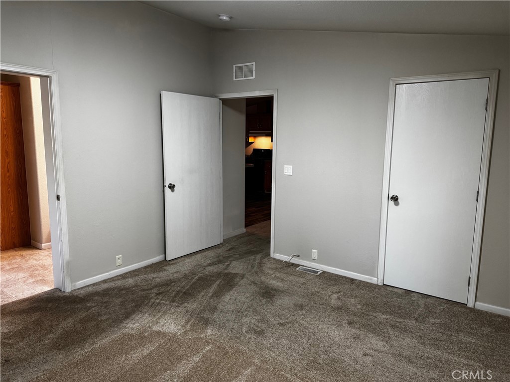 Empty carpeted room with light gray walls, two white doors, and an open doorway.