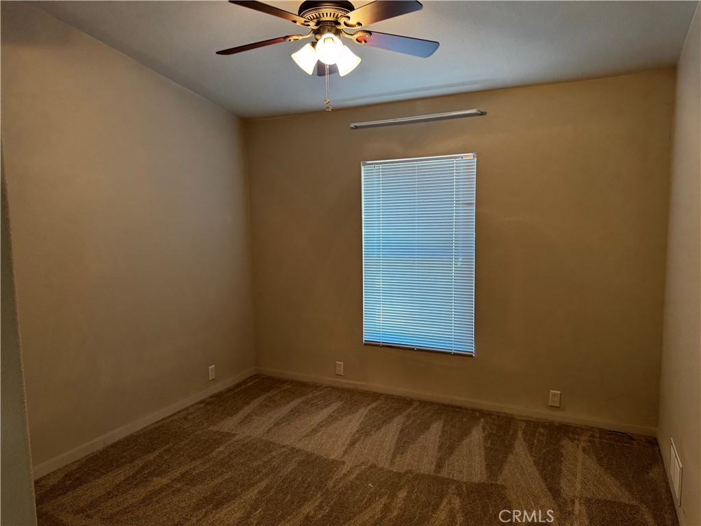 Empty carpeted bedroom with closed window blinds and a ceiling fan with light.